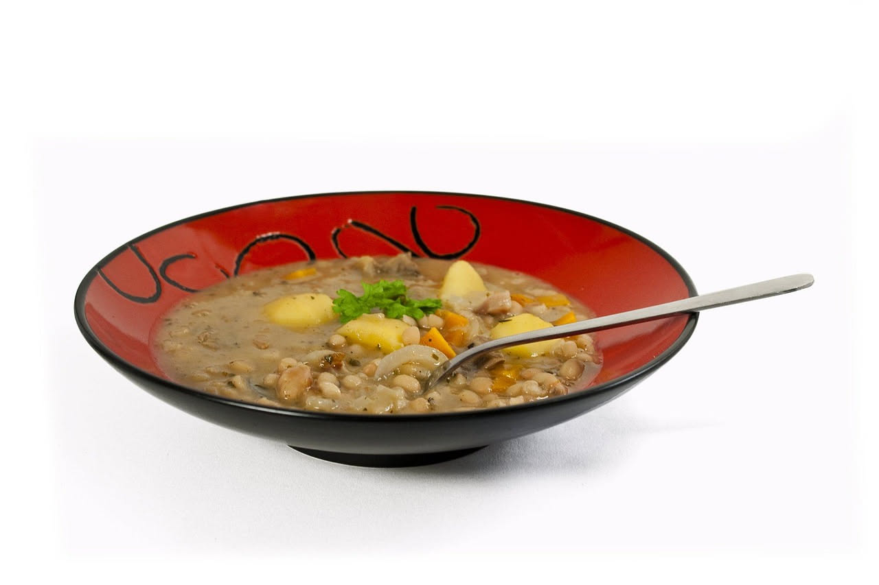 Ciotola di ceramica bianca con jota fredda: fagioli bianchi e rossi, crauti chiari, peperoncino rosso affettato, brodo trasparente color ambra, servita con ghiaccio intorno al piatto